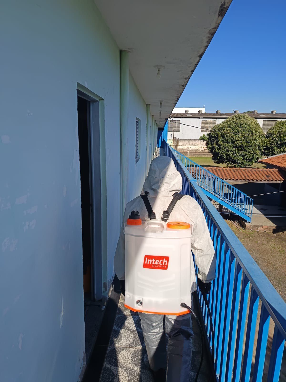 Técnico com pulverizador costal aplicando produto em corredor externo de prédio