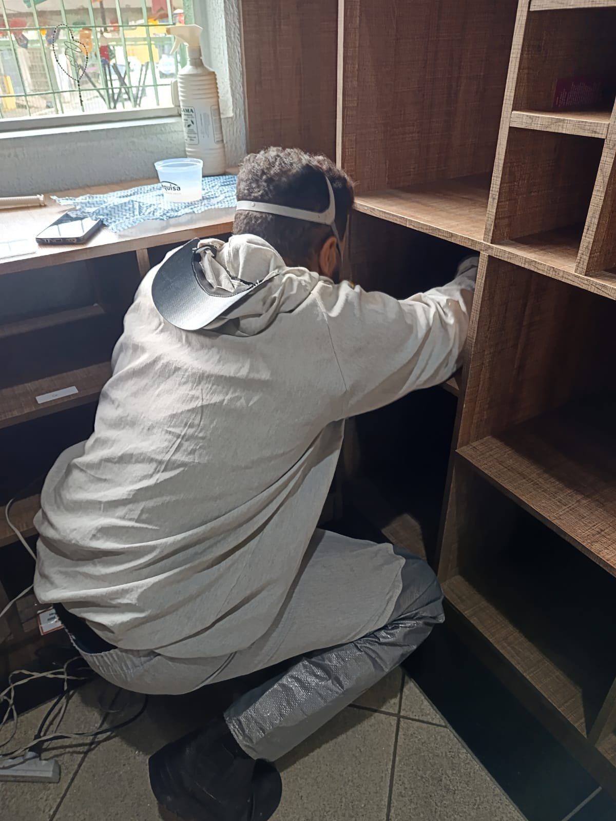 Técnico com protetor facial aplicando produto em prateleiras de madeira