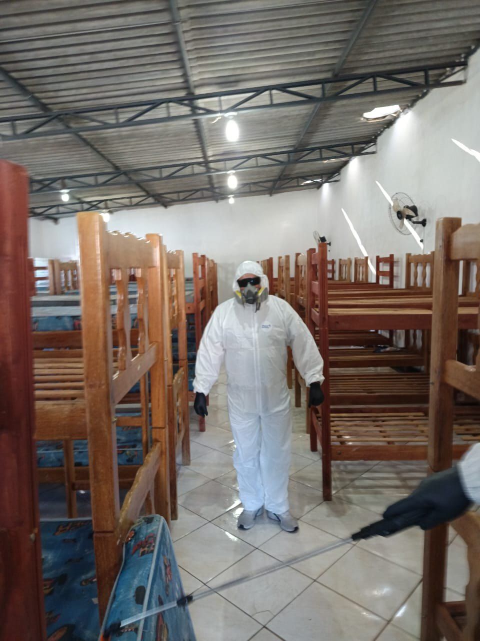 Técnico com máscara de proteção em dormitório com beliches durante a aplicação