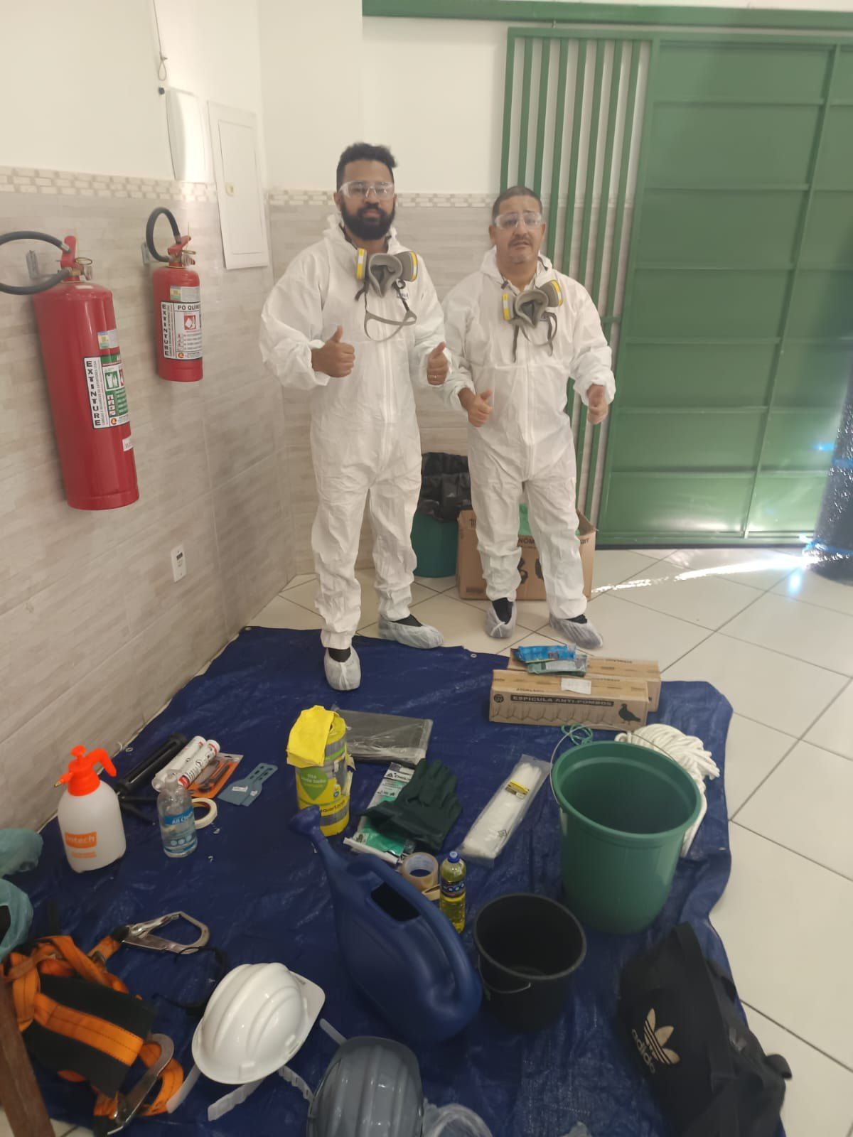 Equipe da Elite Ambiental vestida com macacão e máscara de proteção, com o material de trabalho organizado no chão